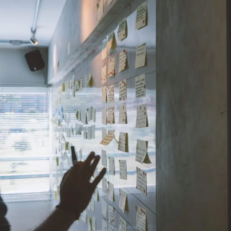 Person heftet Notizzettel an eine Wand voller Haftnotizen